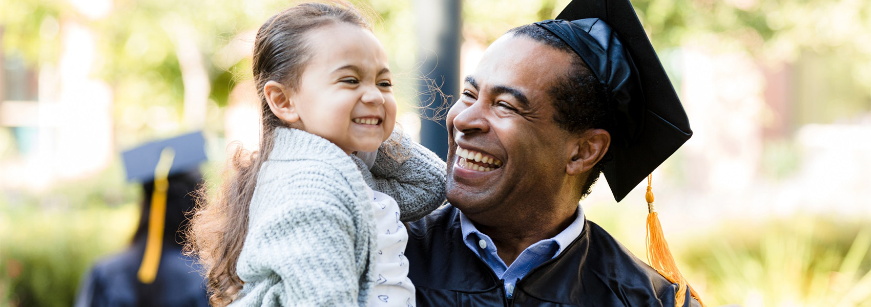 A smiling man in a cap and gown holding a little girl in his arms